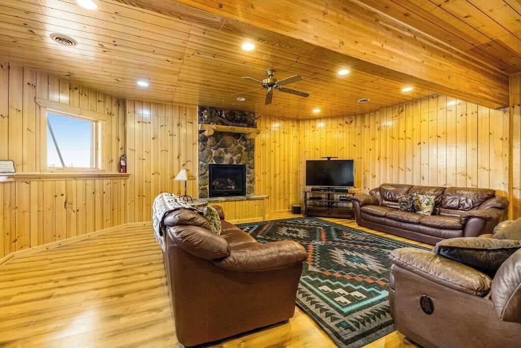A wooden-paneled room with a fireplace, leather sofas, and a flat-screen TV.