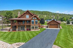 A two-story house with a covered porch, a garage, and a driveway leading to the entrance. - Reunion Lodge • Hot Tub, Game Room & Views (Sturgis)