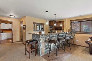 A kitchen with a stone island, bar stools, pendant lighting, and wooden cabinets. - Reunion Lodge - Hot Tub, Game Room & Views (Sturgis)