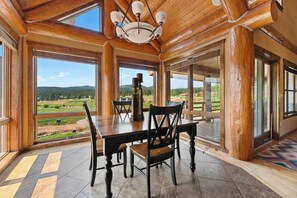 A wooden interior with a dining table and chairs, large windows with a view of a landscape, and a chandelier. - Reunion Lodge - Hot Tub, Game Room & Views (Sturgis)