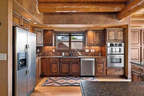 A kitchen with wooden cabinets, stainless steel appliances, and a window above the sink. - Reunion Lodge - Hot Tub, Game Room & Views (Sturgis)