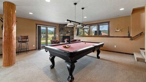 Une table de billard dans une pièce avec un mur en pierre, une cheminée et une vue sur l’extérieur.