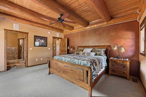 A bedroom with a wooden ceiling, a bed with patterned bedding, a nightstand, and a wall-mounted lamp. - Reunion Lodge - Hot Tub, Game Room & Views (Sturgis)