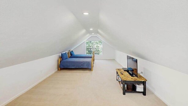 Um quarto de sótão pequeno com teto inclinado, uma cama de solteiro, uma escrivaninha e uma janela que oferece luz natural.