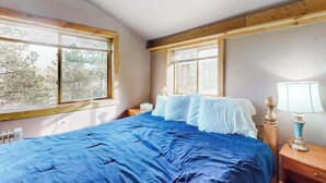 A bedroom with a large bed, two bedside tables, a window, and a view of trees. - Friends & Family Base Camp - Dog-Friendly 3-Story Group Getaway (Woodland Park)