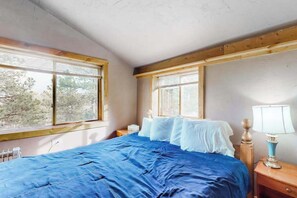 Ein Schlafzimmer mit einem großen Bett, zwei Nachttischen, einem Fenster und Blick auf Bäume.
