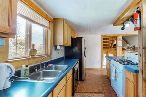 A kitchen with wooden cabinets, a blue countertop, a stainless steel sink, a refrigerator, a stove, and a window with a view of the outdoors. - Friends & Family Base Camp - Dog-Friendly 3-Story Group Getaway (Woodland Park)