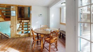 A dining area with a round wooden table and chairs, a wooden staircase, and a window with blinds. - Friends & Family Base Camp - Dog-Friendly 3-Story Group Getaway (Woodland Park)