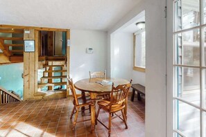 Ein Essbereich mit einem runden Holztisch und Stühlen, einer Holztreppe und einem Fenster mit Jalousien.