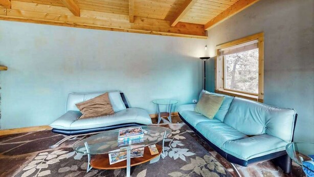 A living room with a wooden ceiling, a light blue sofa, a glass coffee table, and a window with a view. - Friends & Family Base Camp - Dog-Friendly 3-Story Group Getaway (Woodland Park)