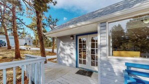 A wooden deck with a blue railing, a white building with a blue door, and a clear sky. - Friends & Family Base Camp - Dog-Friendly 3-Story Group Getaway (Woodland Park)