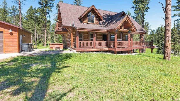 Eine Blockhütte mit Veranda, umgeben von einer Rasenfläche und hohen Bäumen.
