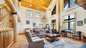 Ein geräumiges Wohnzimmer mit einer großen Eckcouch, einem Couchtisch und einem Kamin. Mehrere Fenster sorgen für natürliches Licht und Blick ins Freie.