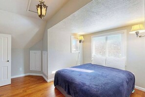 Ein Schlafzimmer mit einem Bett, einem Fenster mit Jalousien, einer Tür und einer Deckenleuchte.