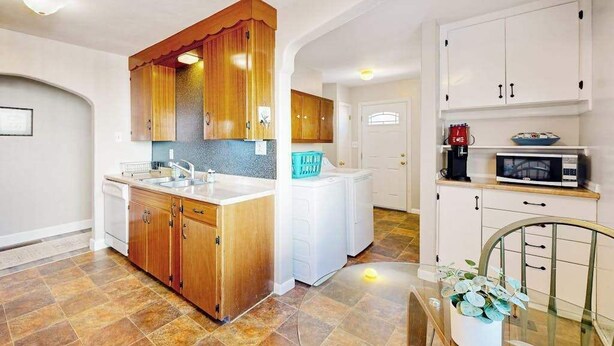 Una cocina con armarios de madera, encimera blanca, un lavabo, un microondas y una lavadora blanca.