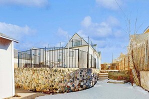 Una casa moderna con un muro de piedra, una cerca de metal y un cielo despejado.