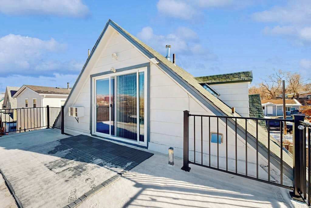Una casa moderna de un solo piso con un amplio ventanal corredero, un porche cubierto y una cerca de metal negro.