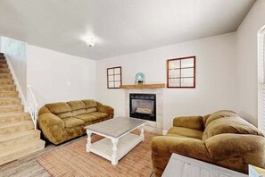 A living room with a fireplace, two sofas, a coffee table, and a staircase. - Sunflower Way - Dog-Friendly Home • Mountain Views (Colorado Springs)