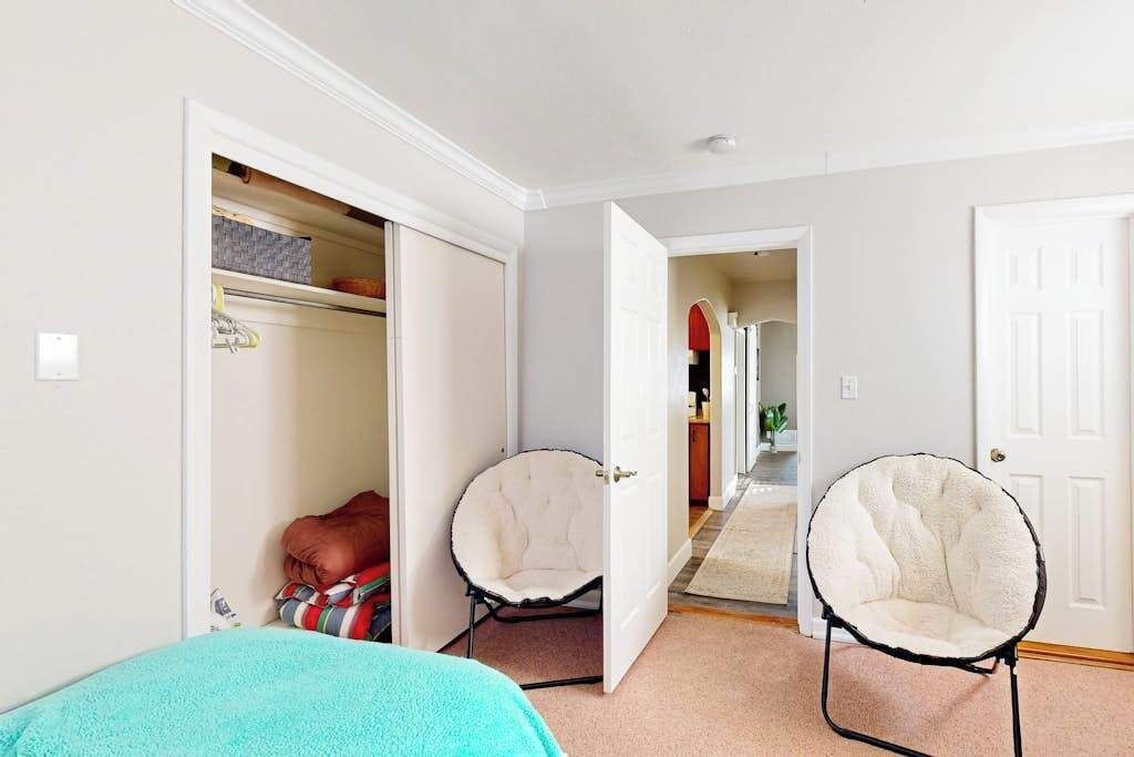 A hallway with a closet, two chairs, and a door leading to another room.