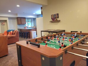 Ein Wohnzimmer mit Kicker, einer Couch und einer dahinterliegenden Küchenzeile.