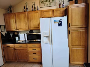 Eine Küche mit Holzschränken, einem weißen Kühlschrank, einer Mikrowelle und einem Wasserspender.