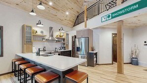 A modern kitchen with a central island, bar stools, and a staircase leading to an upper level. - Sundby Cabin - New Chalet • Walk to Skiing (Lead)