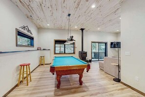 Ein Billardtisch in einem Raum mit Holzdielenboden, Deckenbalken und einem Kamin.