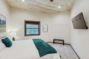 Ein Schlafzimmer mit Bett, Fenster, Bank und einem an der Wand montierten Fernseher.