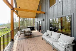 Eine Holzterrasse mit Sofa und Tisch, mit Blick auf einen bewaldeten Bereich.