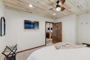 Un dormitorio con cama, ventilador de techo, televisor montado y una puerta que da a otra habitación.