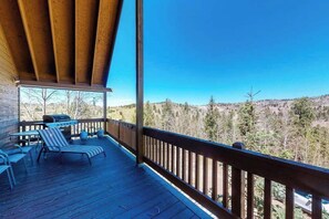 Eine überdachte Terrasse im Freien mit Liegestühlen und einem Grill, mit Blick auf eine bewaldete Landschaft.