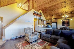 A spacious living room with a high ceiling, a staircase, a kitchen in the background, and a sofa. - Timberline Vista - Secluded Mountain Escape (Cripple Creek)