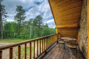 A wooden deck with a railing, a table with chairs, and a view of a forested area. - Tetro Rock Retreat - Game Room & Forest Views (Deadwood)