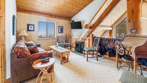 En hyggelig loftstue med skråvægge, pejs, sofa, bord og fjernsyn.