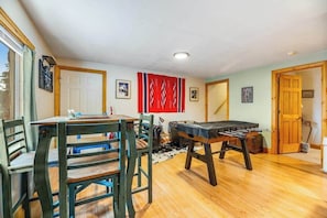 A room with a wooden table and chairs, a foosball table, and a red patterned wall hanging. - Tetro Rock Retreat - Game Room & Forest Views (Deadwood)