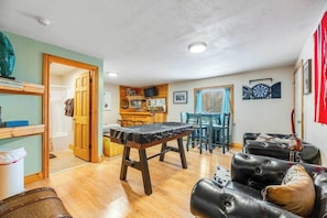 A living room with a foosball table, a dining area with chairs, and a kitchen in the background. - Tetro Rock Retreat - Game Room & Forest Views (Deadwood)