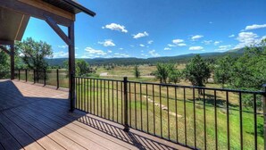 Eine Holzterrasse mit Metallgeländer, die auf eine ländliche Landschaft mit Bäumen und Hügeln blickt.