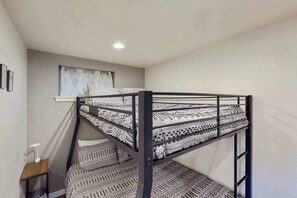 A bunk bed with patterned bedding, a window with curtains, a small table with a lamp, and a wall-mounted shelf. - The Trailhead - Mtn-View Apt • Hot Tub, Dogs OK (Green Mountain Falls)