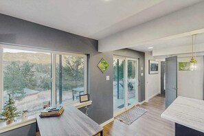 A modern interior with large windows, a wooden desk, and a view of the outdoors. - The Trailhead - Mtn-View Apt • Hot Tub, Dogs OK (Green Mountain Falls)