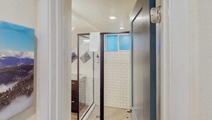 A hallway leading to a bathroom with a glass door, a tiled shower area, and a painting on the wall. - Mtn-View Apt • Private Hot Tub, Dogs OK (Green Mountain Falls)