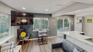A modern kitchen with a dining area, a sofa, and a TV mounted on the wall. - Mtn-View Apt • Private Hot Tub, Dogs OK (Green Mountain Falls)