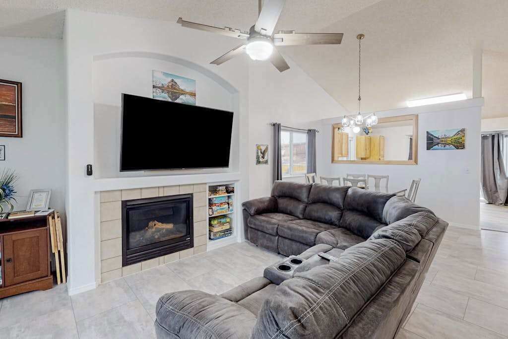 A living room with a fireplace, a large flat-screen TV, a grey sofa, and a ceiling fan.