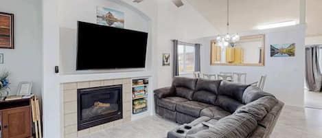 Una sala de estar con chimenea, un televisor de pantalla plana grande, un sofá gris y un ventilador de techo.