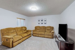 A living room with two sofas, a television, and a window with blinds. - Springs Manor - Dog-Friendly Home • Sunset Mtn Views (Colorado Springs)