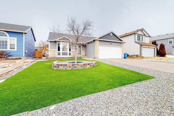 A residential area with houses, a well-maintained lawn, and a circular stone feature. - Springs Manor - Dog-Friendly Home • Sunset Mtn Views (Colorado Springs)