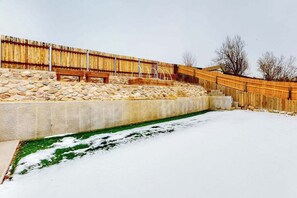 A snow-covered outdoor area with a concrete retaining wall, wooden fence, and a bench. - Springs Manor - Dog-Friendly Home • Sunset Mtn Views (Colorado Springs)