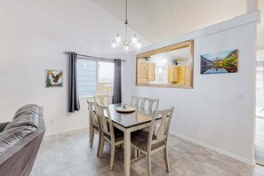 A dining area with a table and chairs, a chandelier, a window with curtains, and a painting on the wall. - Springs Manor - Dog-Friendly Home • Sunset Mtn Views (Colorado Springs)