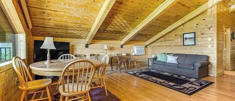 A cozy wooden cabin interior with a dining area, a sofa, and a fireplace.
