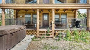 A two-story log cabin with a covered porch, a hot tub, and a fenced outdoor area. - Waterwheel Retreat - Classic Home • Hot Tub & Cozy Loft (Sturgis)