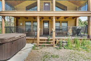 A two-story log cabin with a covered porch, a hot tub, and a fenced outdoor area. - Waterwheel Retreat - Classic Home • Hot Tub & Cozy Loft (Sturgis)